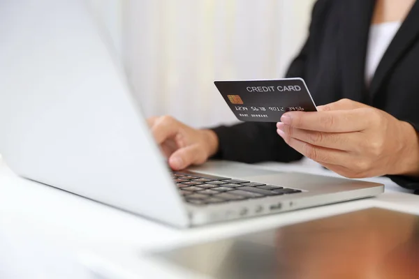 Woman hands in black suit sitting and holding credit card and using laptop computer on table for online payment or shopping online. Business woman using internet while working. E-Banking concept