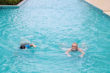 Mutlu Kafkasyalı koca ve yaşlı Asyalı eş güneşli bir günde emeklilik tatilinde havuzda yüzüyor. 