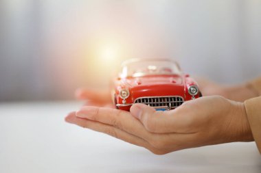 Genç aktif iş kadını, beyaz masada araba modelini ya da otomobili tutarken ve korurken rahat elbiseler giyiyor. Sigorta ve güvenlik kavramı