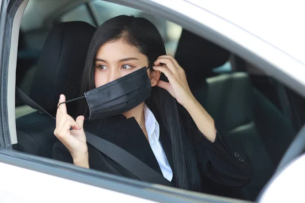 Young asian healthy woman in business black suit wearing protect mask for healthcare in automobile and driving car. New normal and social distancing concept