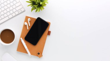 Üzerinde bilgisayar ve ofis malzemeleri olan beyaz manzaralı ahşap ofis masası. Boş defter, klavye, yeşil yaprak ve kahve fincanı olan düz bir çalışma masası. Reklam içeriğiniz için alanı kopyalayın.