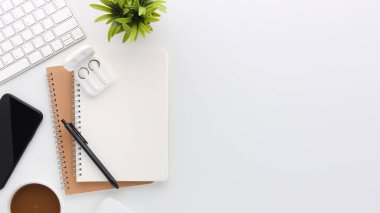 Üzerinde bilgisayar ve ofis malzemeleri olan beyaz manzaralı ahşap ofis masası. Boş defter, klavye, yeşil yaprak ve kahve fincanı olan düz bir çalışma masası. Reklam içeriğiniz için alanı kopyalayın.