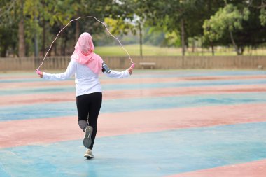 Dikiz ayarı atletik genç Asyalı müslüman kadın spor giyim ayakta duruyor ve sabah egzersizi için ip atlıyor. Aktif kız, ağaç köklü pazı egzersizi yapıyor. Spor konsepti