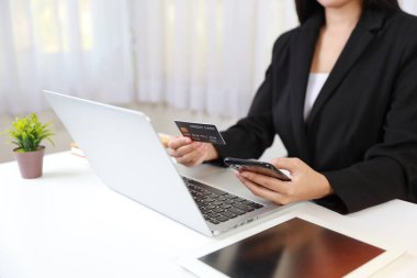 Kadın elleri oturuyor ve akıllı telefon tutuyor ve online ödeme veya online alışveriş için kredi kartı ve tablet kullanıyor. İş kadını çalışırken internet kullanıyor. E-Bankacılık kavramı