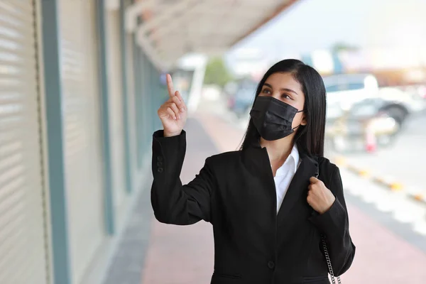 Young asian business woman in business black suit with protect mask for healthcare walking on street public outdoor and pointing something. New normal and social distancing concept