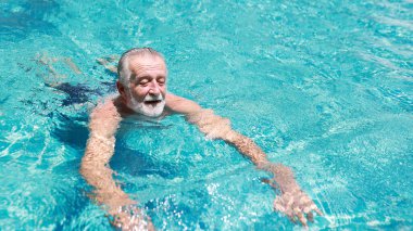 Emeklilik tatilinde havuzda yüzen mutlu, yaşlı, beyaz bir adam. Rahatlama ve gülümsemeyle.