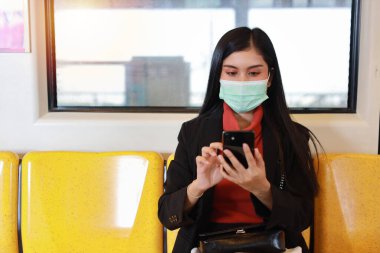 Yeni normal covid-19 salgını. Trendeki insanlardan virüs kapmasını önlemek için maske takan Asyalı genç bir kadın. Trende akıllı telefon iletişimi kullanıyor.