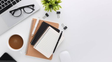 Üzerinde bilgisayar ve ofis malzemeleri olan beyaz manzaralı ahşap ofis masası. Boş defter, klavye, yeşil yaprak ve kahve fincanı olan düz bir çalışma masası. Reklam içeriğiniz için alanı kopyalayın.