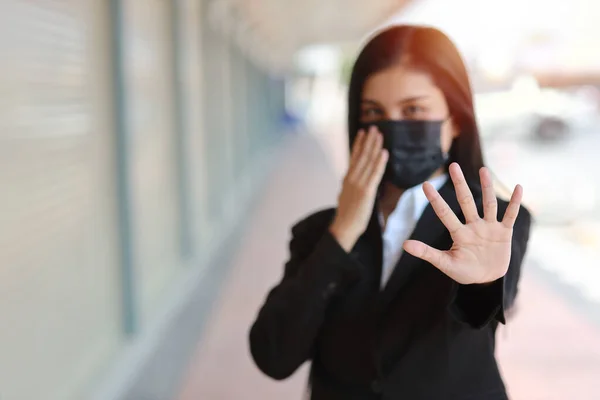 Young asian business woman in business suit with protect mask for healthcare walking on street public outdoor and making stop crossing hands gesture for stop corona virus outbreak. New normal concept