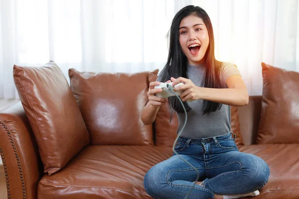 VDO game console station concept. active asian woman sitting on sofa, holding joystick and playing exciting game. Cute girl looked excited with game controller console