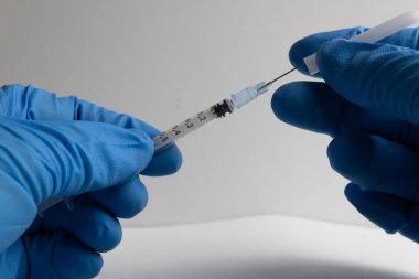 Mavi lateks eldivenli hemşire şırıngayı çıkarıyor.