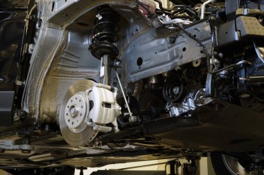 Araba servisinde modern bir araba. Araba tamir edilmek üzere kısmen parçalanmış. Arabanın ön çamurluğu sökülmüş ve süspansiyonun parçaları, fren sistemi ve motorun bir kısmı görünür durumda..