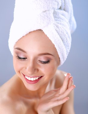 Güzel genç kadın yüzünde gri arka plan üzerinde izole bir krem uygulamak