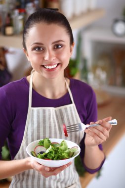 Genç kadın modern mutfakta taze salata yiyor.