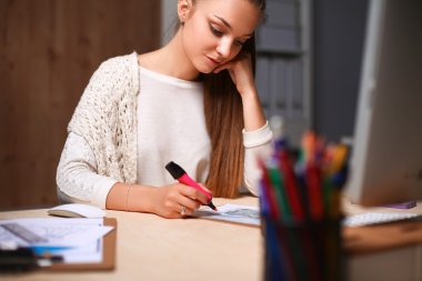 Ofiste çalışan genç bir kadın, masada oturuyor.