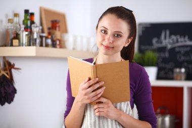 Mutfakta yemek kitabı okuyan genç bir kadın yemek tarifi arıyor.