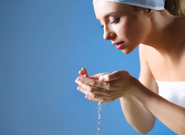 Unga kvinnliga tvätta hennes ansikte med klart vatten — Stockfoto