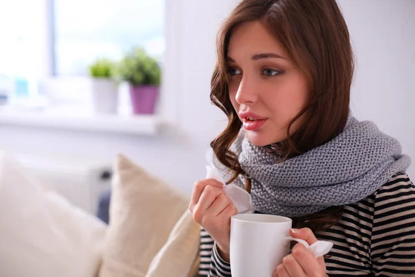 Portrait of a sick woman blowing her nose while sitting on the sofa — Stock Photo, Image