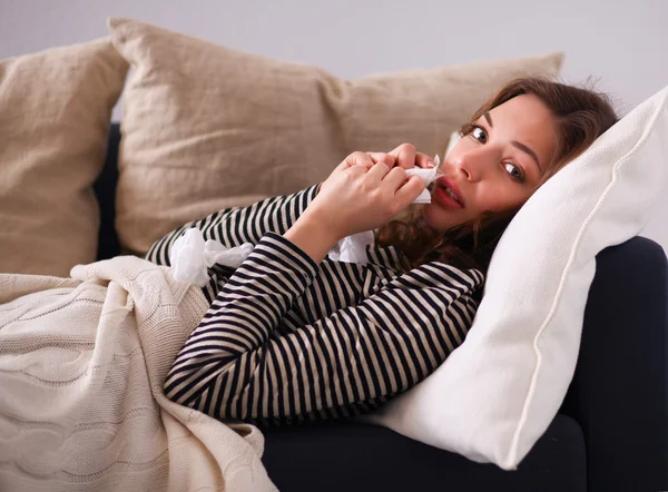 Portrait of a sick woman blowing her nose while sitting on the sofa — Stock Photo, Image