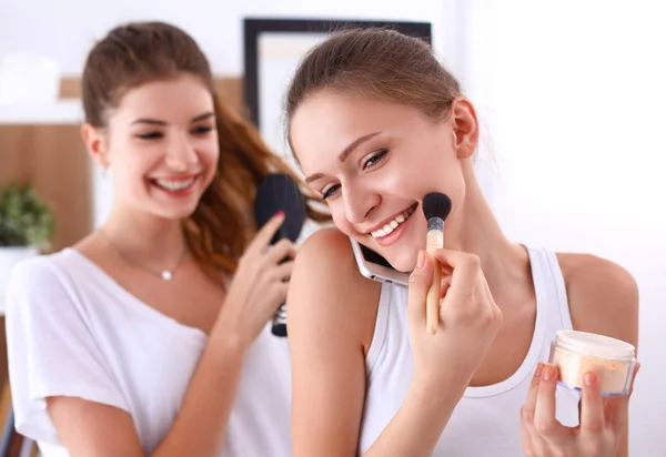 Meninas bonitas olhando no espelho e aplicando cosméticos com uma escova grande — Fotografia de Stock