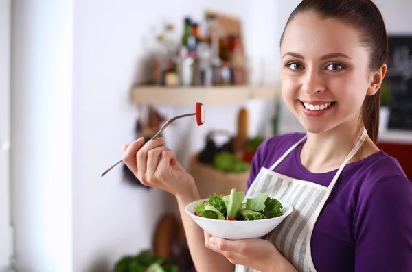 Mujer joven comiendo ensalada fresca en la cocina moderna — Foto de Stock