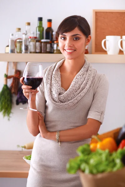 Jovem mulher cortando legumes na cozinha, segurando um copo de vinho — Fotografia de Stock