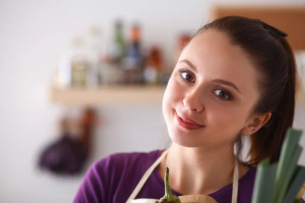 Mujer joven sosteniendo bolsa de la compra de comestibles con verduras de pie en la cocina —  Fotos de Stock