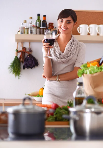 Young woman cutting vegetables in kitchen, holding a glass of wine — Stock Photo, Image