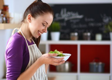 Genç kadın modern mutfakta taze salata yiyor.