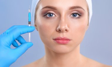 Güzel kadın yüz kozmetik enjeksiyon. Gri arka plan üzerinde izole