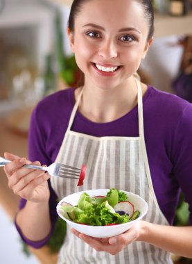 Genç kadın modern mutfakta taze salata yiyor.