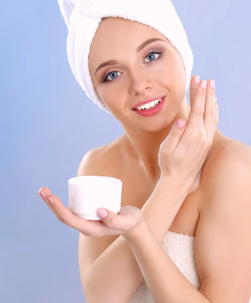 Hermosa joven aplicando una crema en su cara aislada sobre fondo gris — Foto de Stock