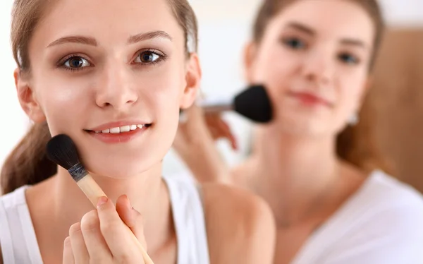 Beautiful girls looking in the mirror and applying cosmetic with a big brush — Stock Photo, Image