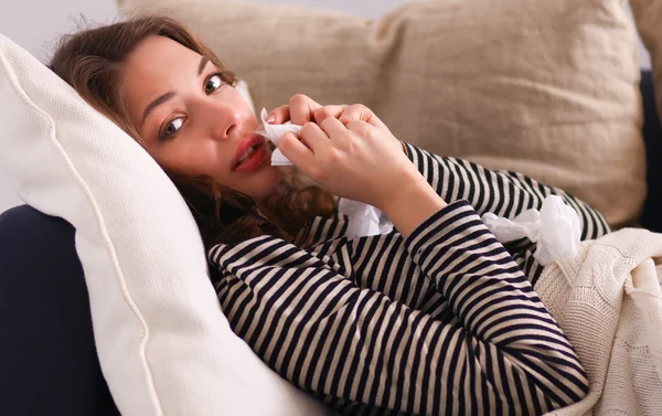 Portrait of a sick woman blowing her nose while sitting on the sofa — Stock Photo, Image