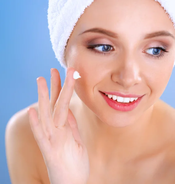 Hermosa joven aplicando una crema en su cara aislada sobre fondo gris — Foto de Stock