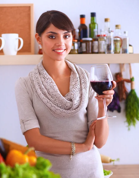 Jeune femme coupant des légumes dans la cuisine, tenant un verre de vin — Photo