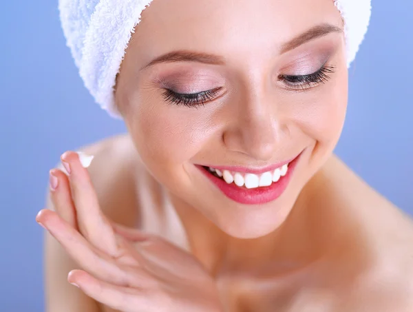 Hermosa joven aplicando una crema en su cara aislada sobre fondo gris —  Fotos de Stock