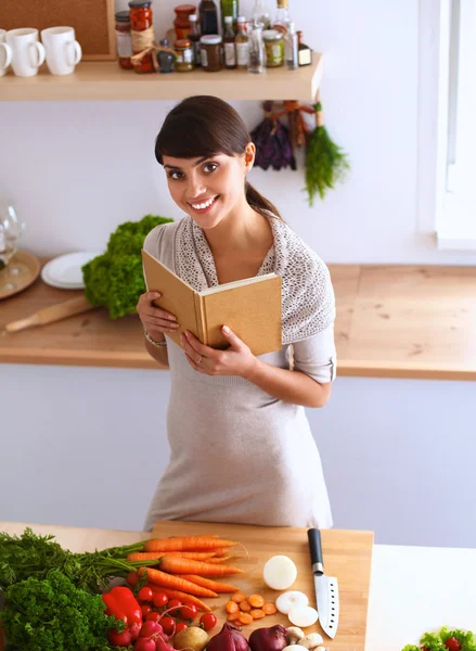 Νεαρή γυναίκα διαβάζει βιβλία μαγειρικής στην κουζίνα, ψάχνει για συνταγή — Φωτογραφία Αρχείου