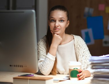 Ofiste çalışan genç bir kadın, masada oturuyor.