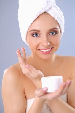 Güzel genç kadın yüzünde gri arka plan üzerinde izole bir krem uygulamak