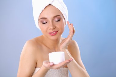 Güzel genç kadın yüzünde gri arka plan üzerinde izole bir krem uygulamak