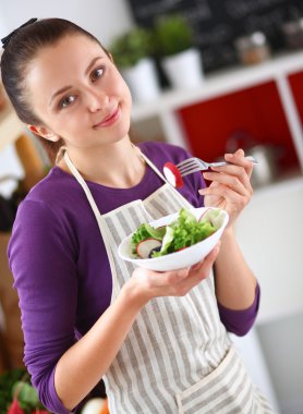 Genç kadın modern mutfakta taze salata yiyor.