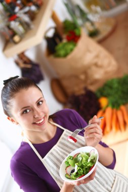 Genç kadın modern mutfakta taze salata yiyor.