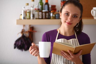 Mutfakta yemek kitabı okuyan genç bir kadın yemek tarifi arıyor.