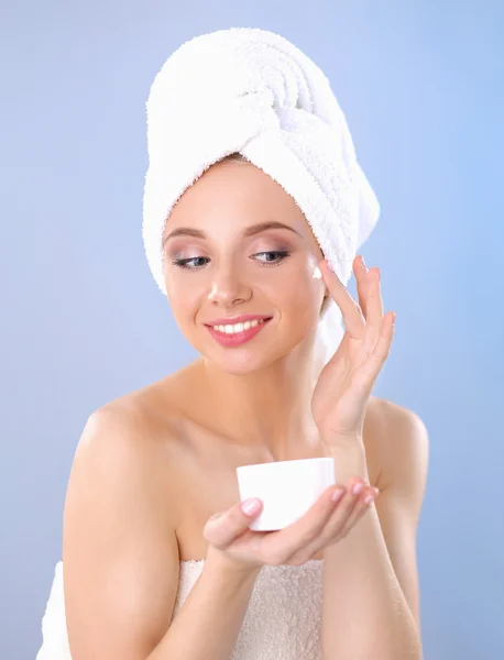 Belle jeune femme appliquant une crème sur son visage isolé sur fond gris — Photo