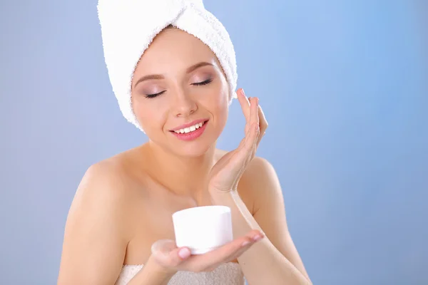 Hermosa joven aplicando una crema en su cara aislada sobre fondo gris —  Fotos de Stock