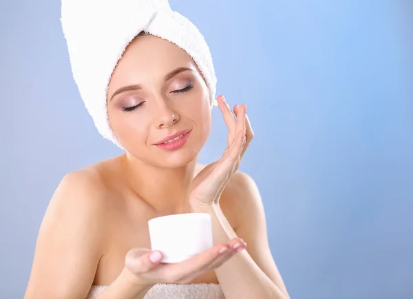 Hermosa joven aplicando una crema en su cara aislada sobre fondo gris — Foto de Stock