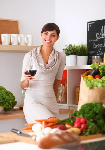 Mujer joven cortando verduras en la cocina, sosteniendo una copa de vino — Foto de Stock