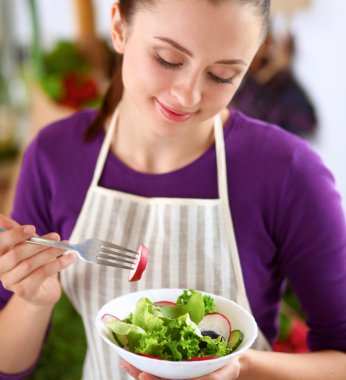 Genç kadın modern mutfakta taze salata yiyor.