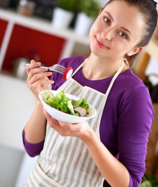 Genç kadın modern mutfakta taze salata yiyor.